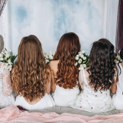 Look from behind at women with hair of different colors sitting on the bed with white tulips