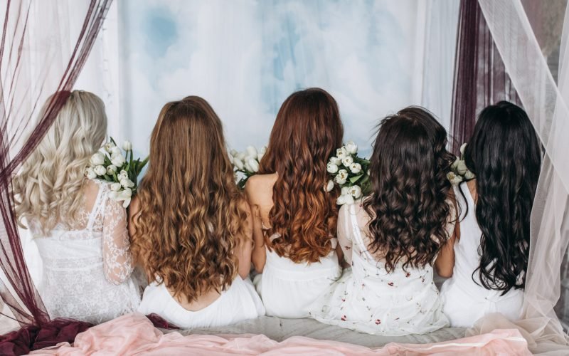 Look from behind at women with hair of different colors sitting on the bed with white tulips